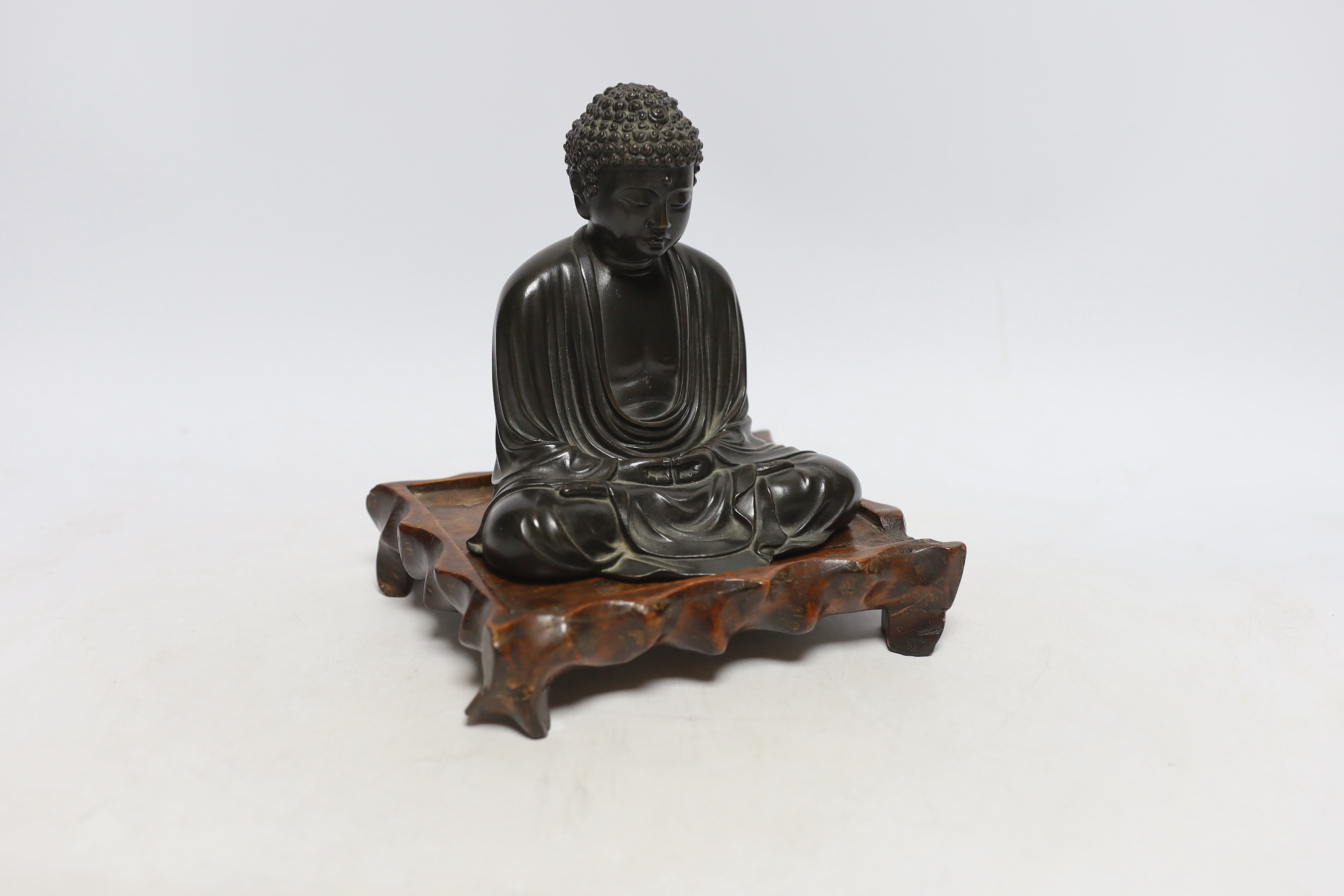 A Japanese bronze figure of Buddha, Meiji period, inscribed seven character mark to base, on a hardwood stand, 15cm high